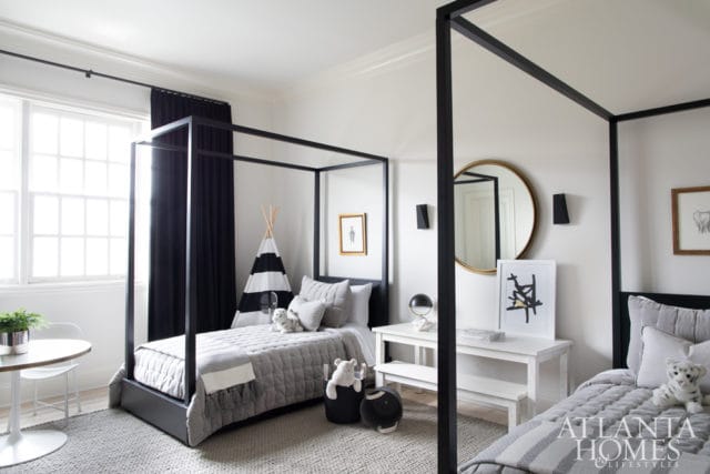 Children's bedroom with two black canopy beds, gray quilted bedding, a striped teepee, and a round gold mirror on the wall.