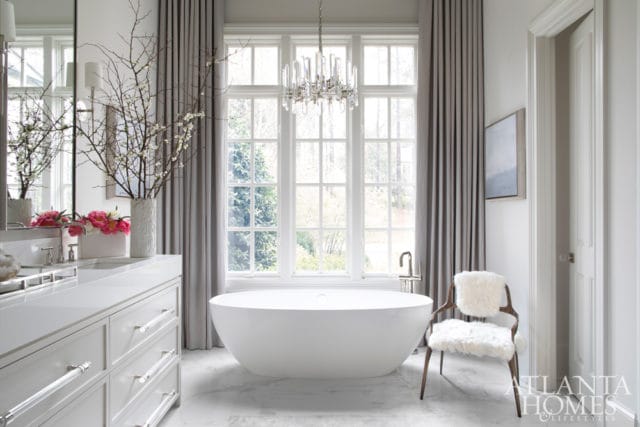 Modern white bathroom with freestanding tub, marble floors, double vanity with crystal drawer pulls, and a crystal chandelier.