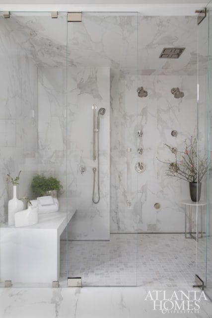 Modern white marble shower with dual shower heads, built-in bench, and glass enclosure. Small mosaic tile floor and chrome fixtures.