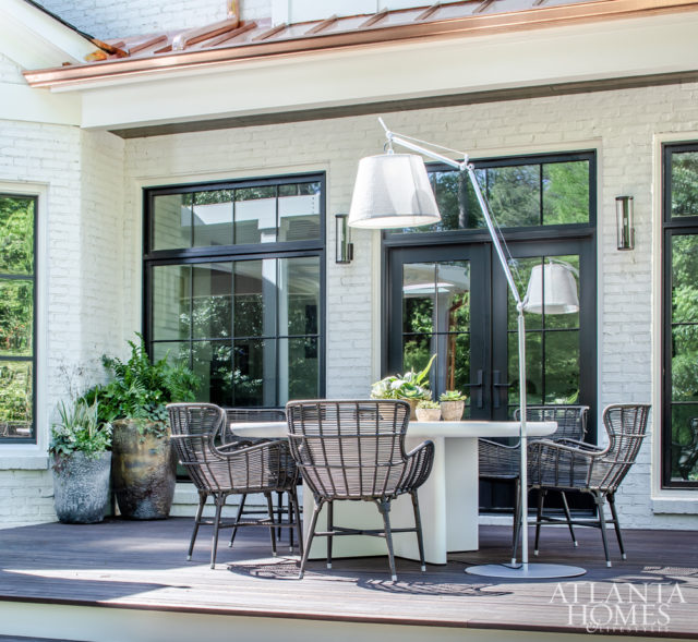 On a dining patio located outside the kitchen, a large lamp by Artemide shines light on a table by Kettal and chairs by Palecek.