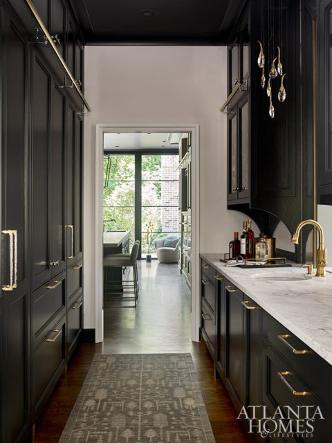 A contemporary pendant light from Ochre by R Hughes plays off of the brass hardware by Matthew Quinn Collection in the butler’s pantry. The rug is Moattar, Ltd.