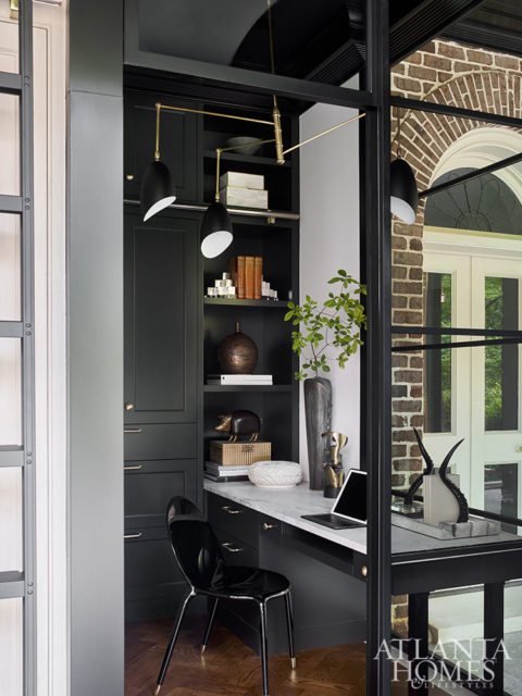 Outfitted with black cabinetry by Design Galleria Kitchen and Bath Studio and illuminated by a midcentury modern-inspired brass chandelier from Circa Lighting, the wife’s office blends classic and contemporary elements.