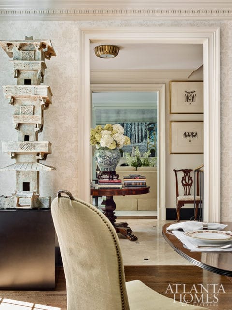 Light beige upholstered dining chair in foreground, looking through doorway to a living room with a sofa and artwork. A decorative pagoda sculpture is on the left.