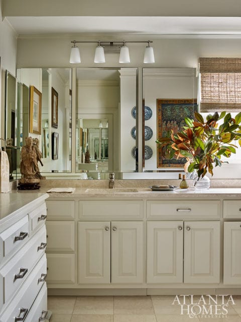 Cream bathroom vanity with marble countertop, double sinks, and brushed nickel hardware. A large mirror reflects artwork and decorative plates on the wall.