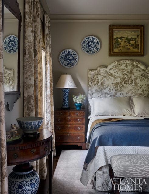 Bedroom with a blue and white patterned headboard, blue blanket, wooden dresser, and decorative blue and white plates on the wall.