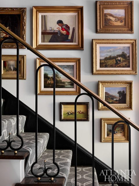Staircase with patterned runner and black railing adorned with framed paintings of landscapes and figures.