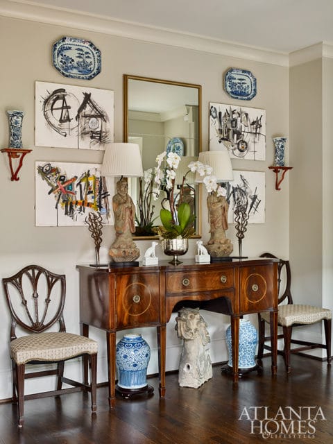 Entryway with a mahogany console table, two chairs, abstract art, blue and white porcelain vases, and a mirror.