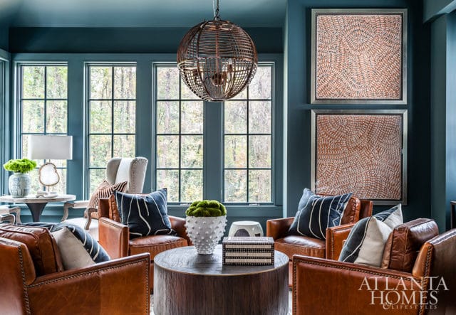 Living room with teal walls, leather armchairs, dark wood coffee table, and large windows overlooking a forest.