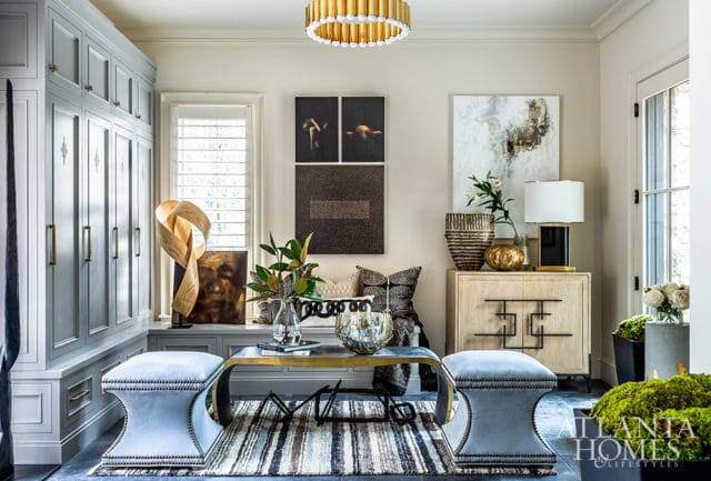 Living room with light gray built-in cabinetry, upholstered benches, a metal coffee table with a striped rug, and abstract art on the walls.