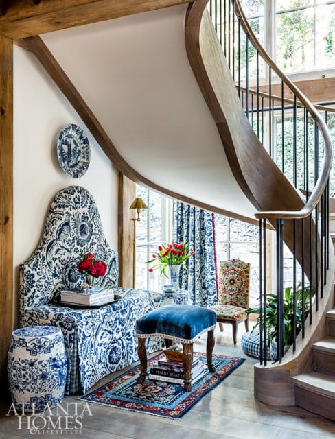 Entryway with a curved wooden staircase, blue and white patterned upholstery on a bench and headboard, a blue velvet stool, a ceramic garden stool, and a Persian rug.