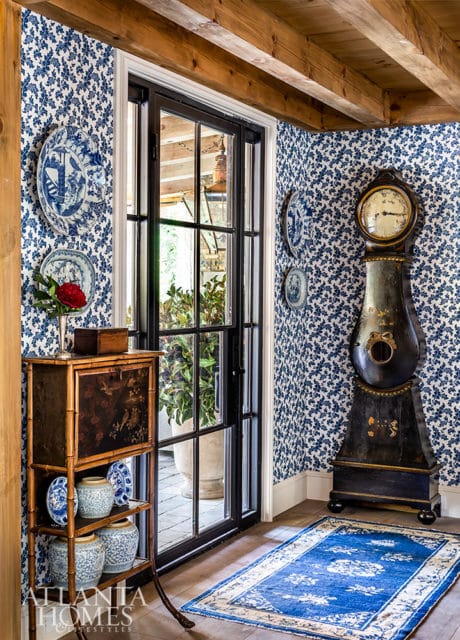 Hallway with blue and white floral wallpaper, a tall antique grandfather clock, a bamboo cabinet with blue and white vases, and a blue oriental rug.