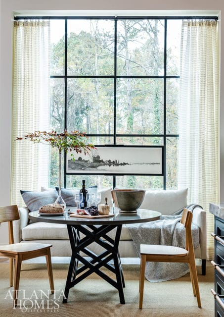 Dining area with a round table set for two, a neutral sofa, and a large grid window overlooking trees.