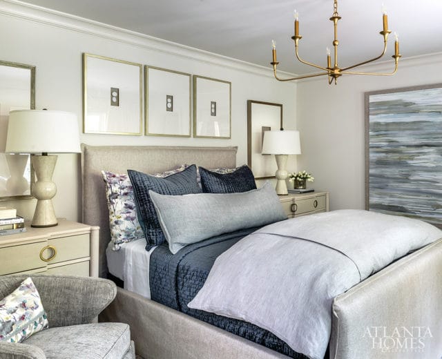 Bedroom with a king-size bed dressed in navy and light blue linens, a tufted headboard, and decorative pillows. A brass chandelier hangs overhead.