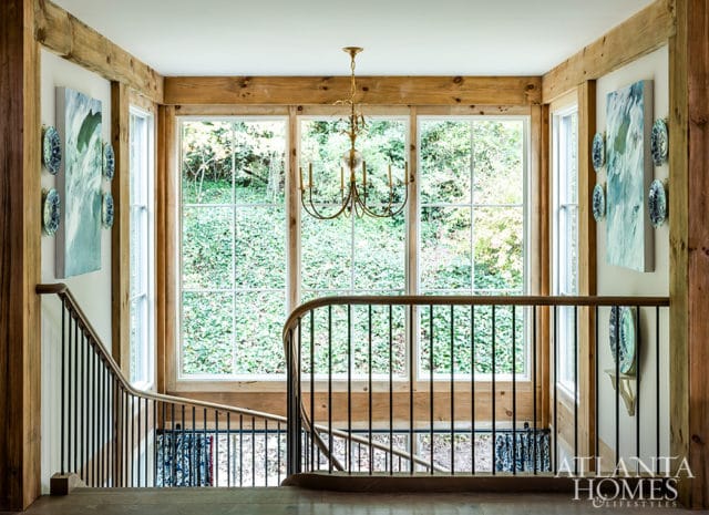 Hallway landing with exposed wooden beams, a curved staircase with black railings, and large windows overlooking greenery.
