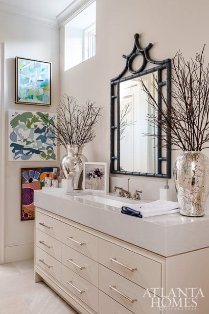 Cream bathroom vanity with a white quartz countertop, silver hardware, and a black pagoda-style mirror. Abstract art hangs on the wall above the vanity.