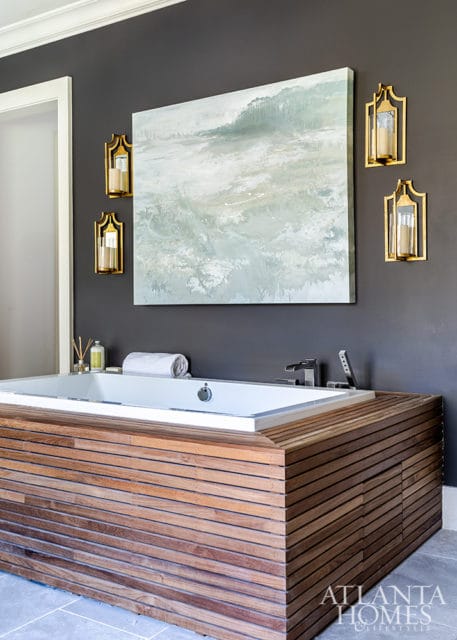 Modern bathroom with a deep soaking tub surrounded by horizontal wood slats, dark gray walls, and abstract landscape art above.