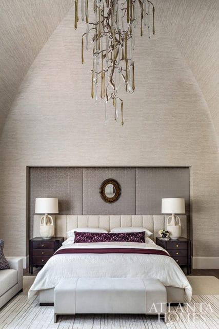 Bedroom with vaulted ceiling featuring textured wallpaper, a large upholstered headboard, and a branch-like chandelier with glass droplets.