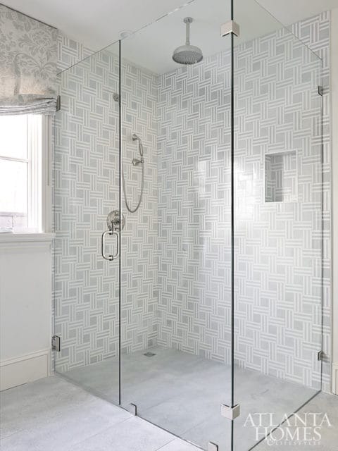 Glass-enclosed shower with geometric patterned tile walls in gray and white, a rainfall showerhead, and a handheld shower fixture.