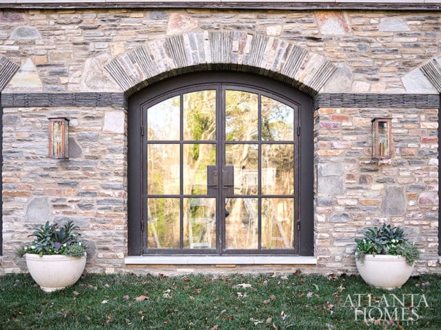 Stone facade with arched metal double doors, flanked by planters and wall lanterns.
