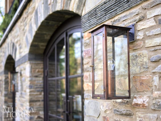 Close-up of a copper lantern with glass panels mounted on a stone wall next to an arched doorway.