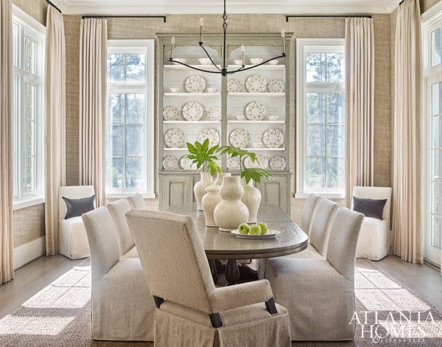 Dining room with oval table, slipcovered chairs, and a tall gray hutch filled with white plates.