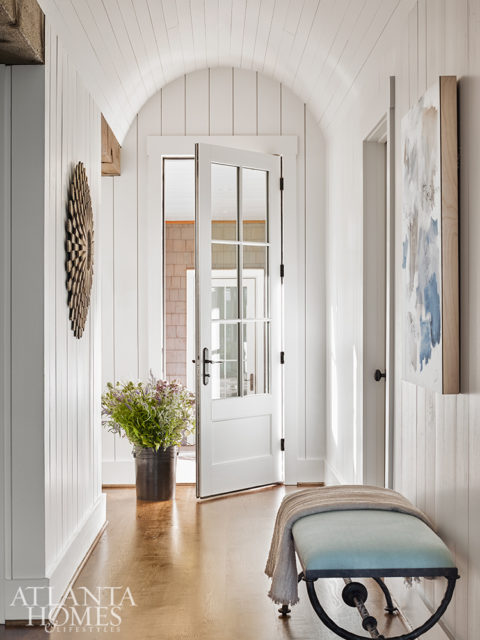 An arched ceiling distinguishes the side entrance, where contemporary artwork and a wood sunburst mirror echo the color palette used throughout the interior.