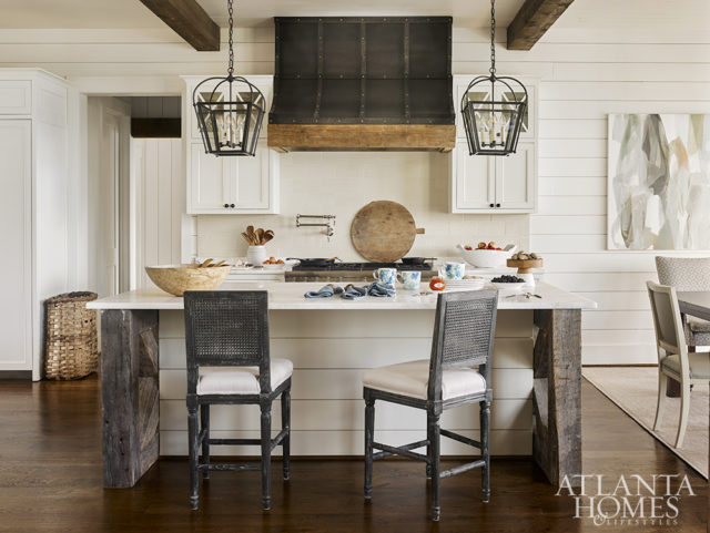 A pair of iron lanterns illuminate the kitchen island, which has a custom x-base made of reclaimed wood that’s topped with marble counters. The barstools are by Bungalow 5 through JDouglas.