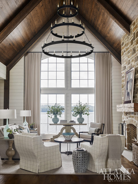 A tall stone fireplace with a reclaimed wood mantel creates a dramatic focal point for a tailored sofa and swivel chairs in the formal living room. The coffee table and console are from Tritter Feefer.