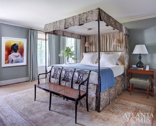 Bedroom with a four-poster bed featuring patterned fabric, light blue bedding, and a dark wood bench with a cane seat. A framed artwork of a woman in traditional Japanese attire hangs on the wall.