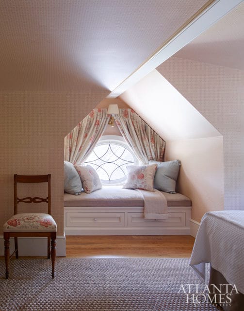 Attic room with pink patterned wallpaper, a built-in window seat with floral curtains, and a wooden chair with floral upholstery.