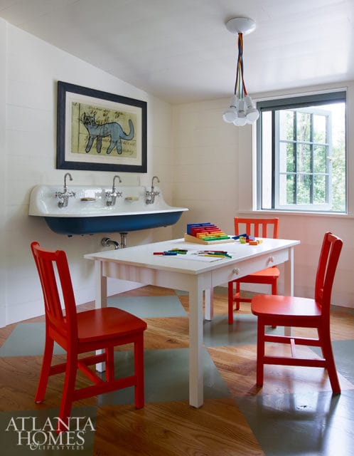 Children's playroom with white table and chairs, vintage blue sink with three faucets, and framed cat artwork on shiplap walls.