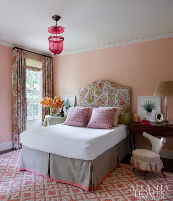 Bedroom with peach walls, a floral upholstered headboard, pink patterned pillows, and a pink geometric rug. A pink glass lantern hangs from the ceiling.