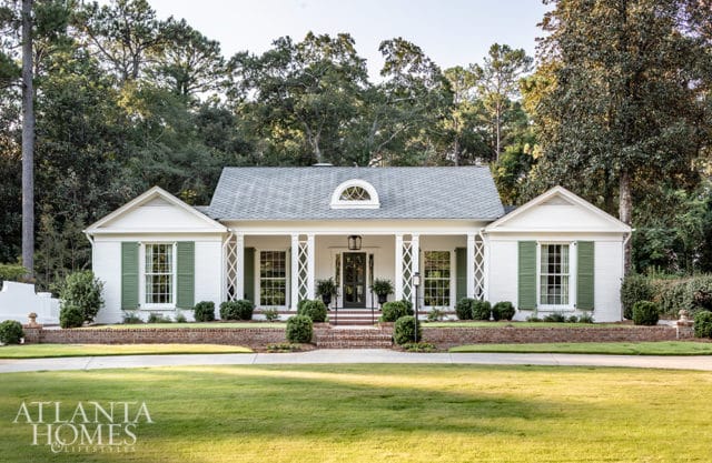 White brick house with green shutters, a covered porch with columns, and a manicured lawn.