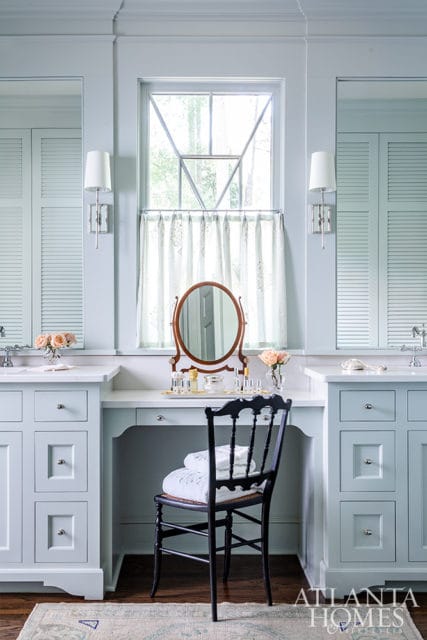 Light blue bathroom vanity with white countertop, a black chair with folded towels, and a vanity mirror surrounded by makeup.