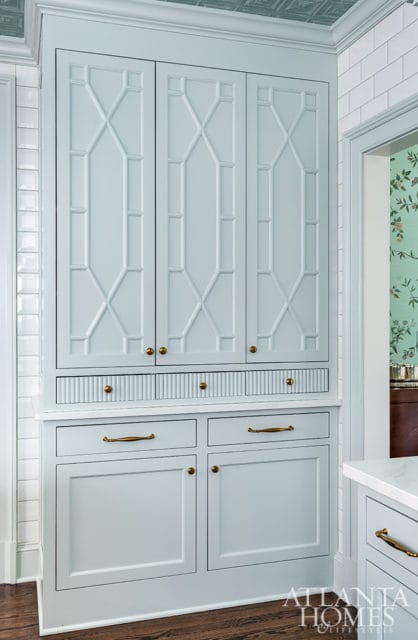 Light blue built-in cabinetry with geometric paneled doors, fluted drawers, and brass hardware. White subway tile backsplash and a patterned ceiling are visible.