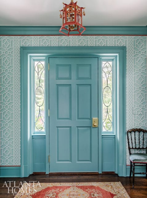 Teal front door with geometric patterned wallpaper in a light blue hue. A red lantern hangs from the ceiling above the door.