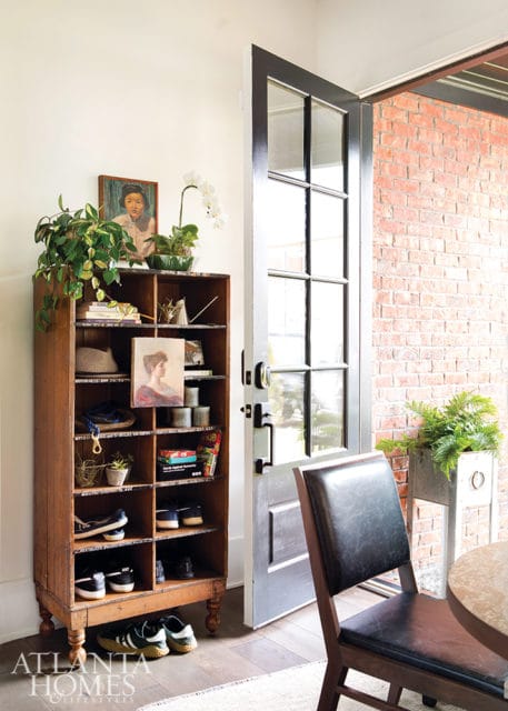 Wooden shoe rack filled with shoes, books, and decorative items next to a gray door opening to a brick patio.