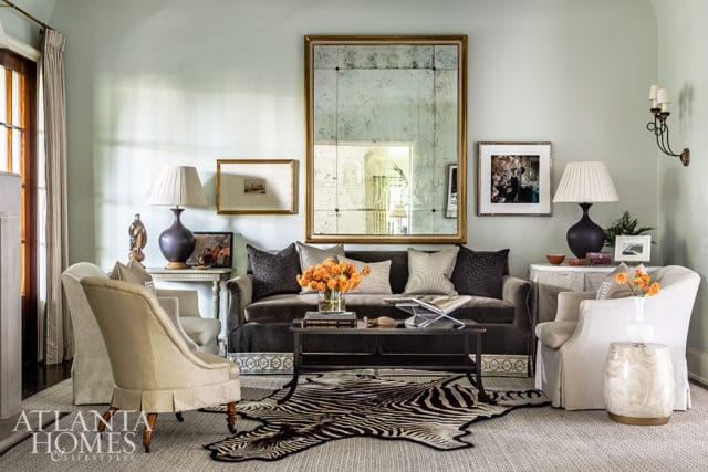 Living room with a dark gray sofa, two cream armchairs, a zebra rug, and a large antique mirror above the sofa.