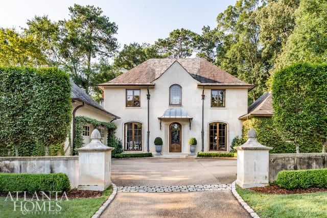 French-inspired stucco home with arched windows, copper awning over the front door, and manicured hedges.
