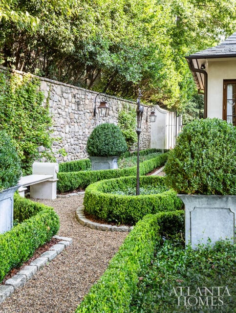 Formal garden with manicured boxwood hedges, gravel paths, stone wall, and decorative urns.