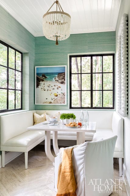 Dining nook with white banquette seating, a white table set for a meal, and grasscloth wallpaper in a light teal hue.