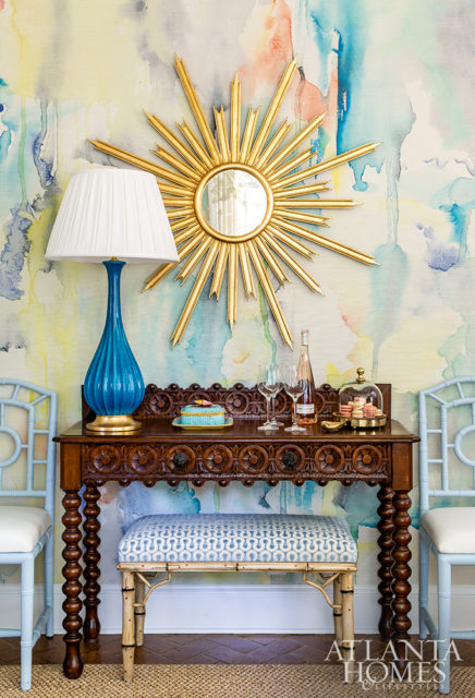 In the dining room, a brilliant symphony of color, periods and styles are represented thanks to a contemporary gilt sunburst mirror, a treasured antique sideboard and Midcentury lamp sourced from Parc Monceau.