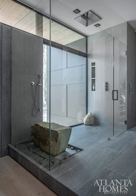 Modern bathroom with a large stone sculpture in a glass-enclosed shower, grey stone tiles, and wood-paneled walls.