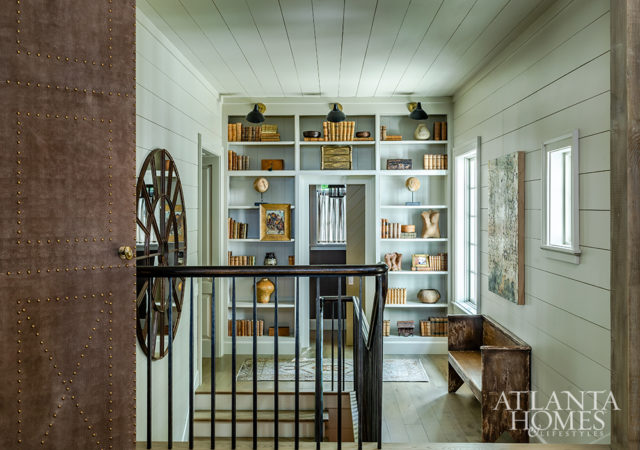 Custom leather doors with nailhead detailing by Burgess separate the kitchen from the stairway landing, where built-in bookshelves surround the entrance to the powder room.