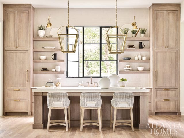 Light wood kitchen with a large island, white subway tile backsplash, open shelving, and brass pendant lights.
