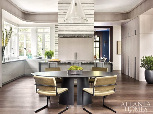 Modern dining area with oval table and four chairs, adjacent to a sleek white kitchen with marble countertops and a large island.