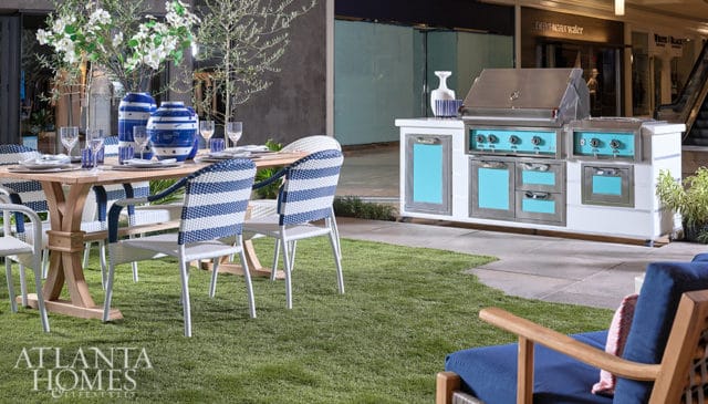 Outdoor dining set with blue and white striped chairs and a wooden table, next to a stainless steel grill with turquoise accents.