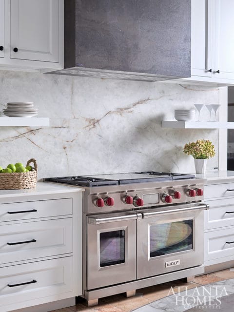 White kitchen with a stainless steel Wolf range, marble backsplash, and white cabinetry.