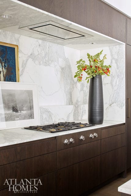 Dark wood cabinetry with marble countertops and backsplash, featuring a gas stovetop, framed artwork, and a tall black vase with greenery and berries.