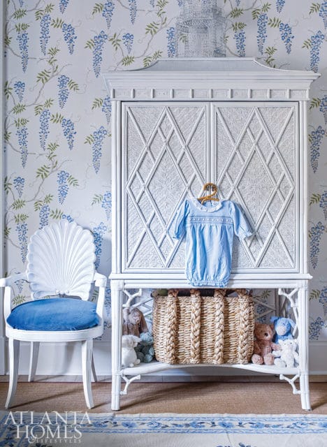 White wicker armoire with diamond pattern doors, a blue baby gown hanging on the front, and a woven basket filled with stuffed animals on the shelf below.